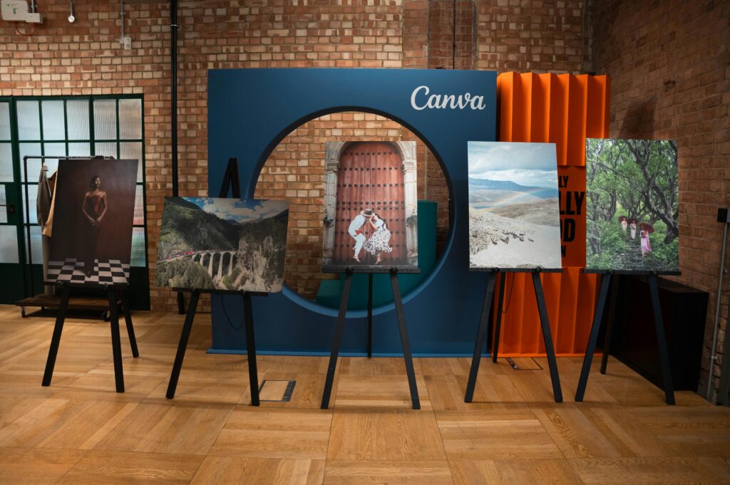 A modern indoor art exhibition showcasing diverse photography on easels against a brick wall.
